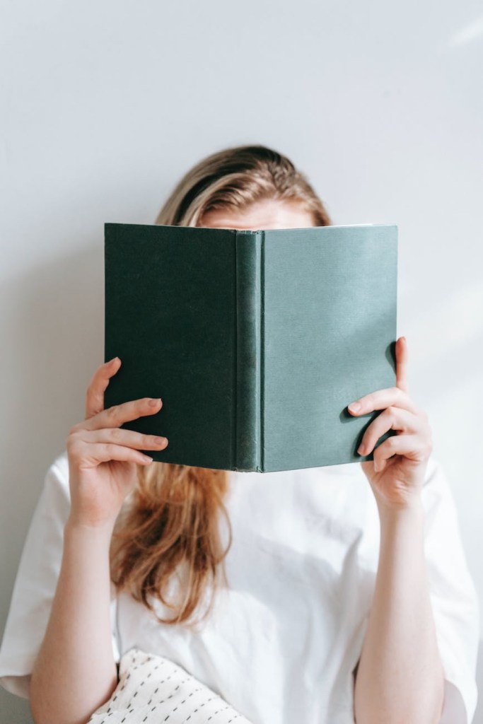 A woman covering her face with a book.